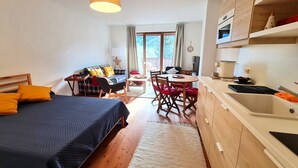 Kompakti hotellihuone, jossa on sänky, pieni ruokapöytä, sohva ja pieni keittiö.