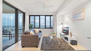 Ein modernes Wohnzimmer mit Sofa, Couchtisch und TV-Möbel. Ein großes Fenster bietet Meerblick und es gibt einen Balkon.