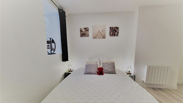 A bedroom with a large bed, a nightstand, a lamp, and a radiator. There are three wall art pieces above the bed. - Beautiful, quiet apartment 5 minutes from Place Stan! (Nancy)