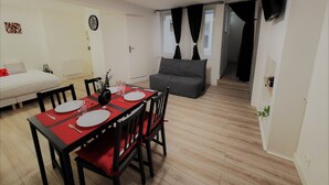 A compact living space with a dining area, a sofa, a TV mounted on the wall, and a clock on the wall. - Beautiful, quiet apartment 5 minutes from Place Stan! (Nancy)