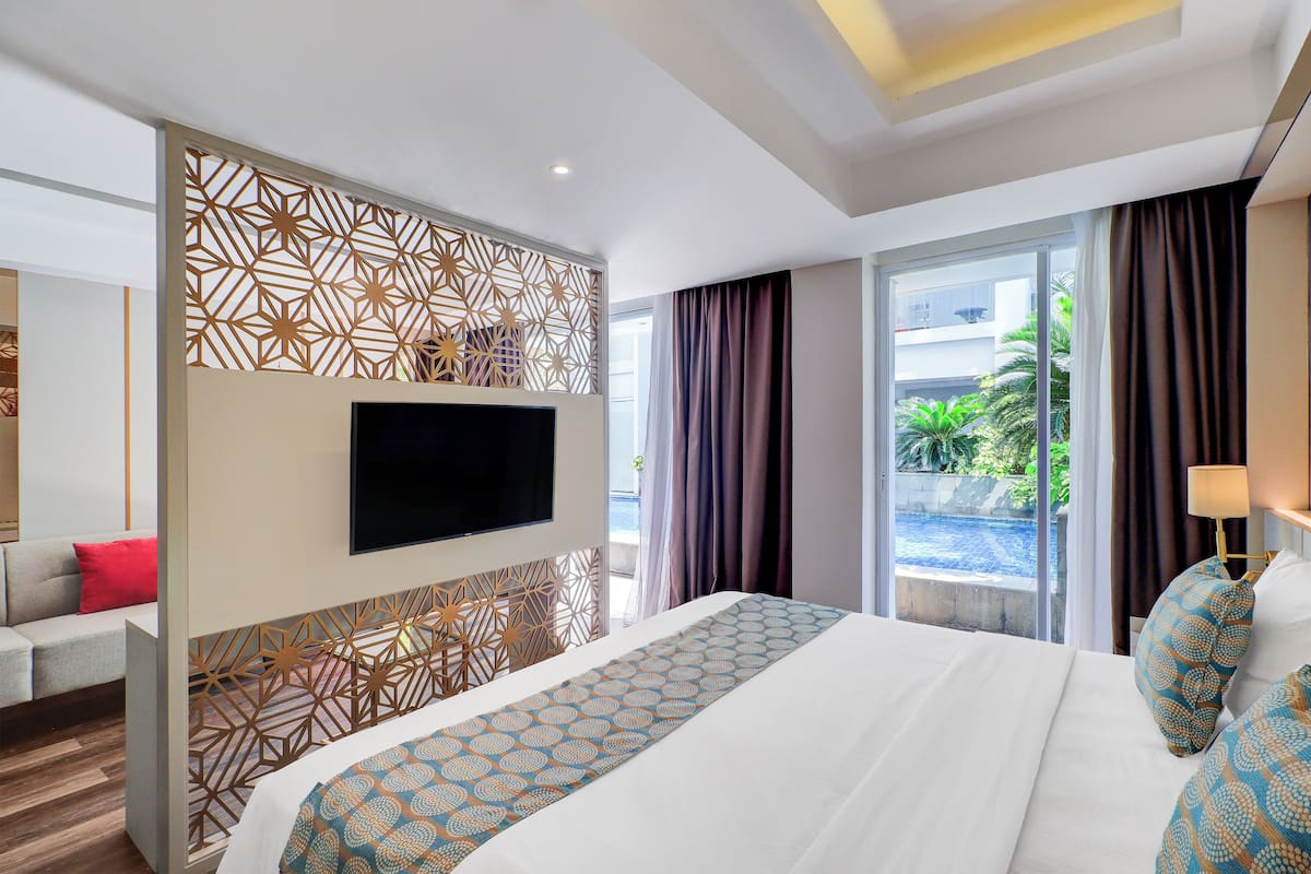 Une chambre d’hôtel avec un grand lit, un téléviseur fixé au mur, un balcon avec des rideaux et une vue sur la verdure environnante.