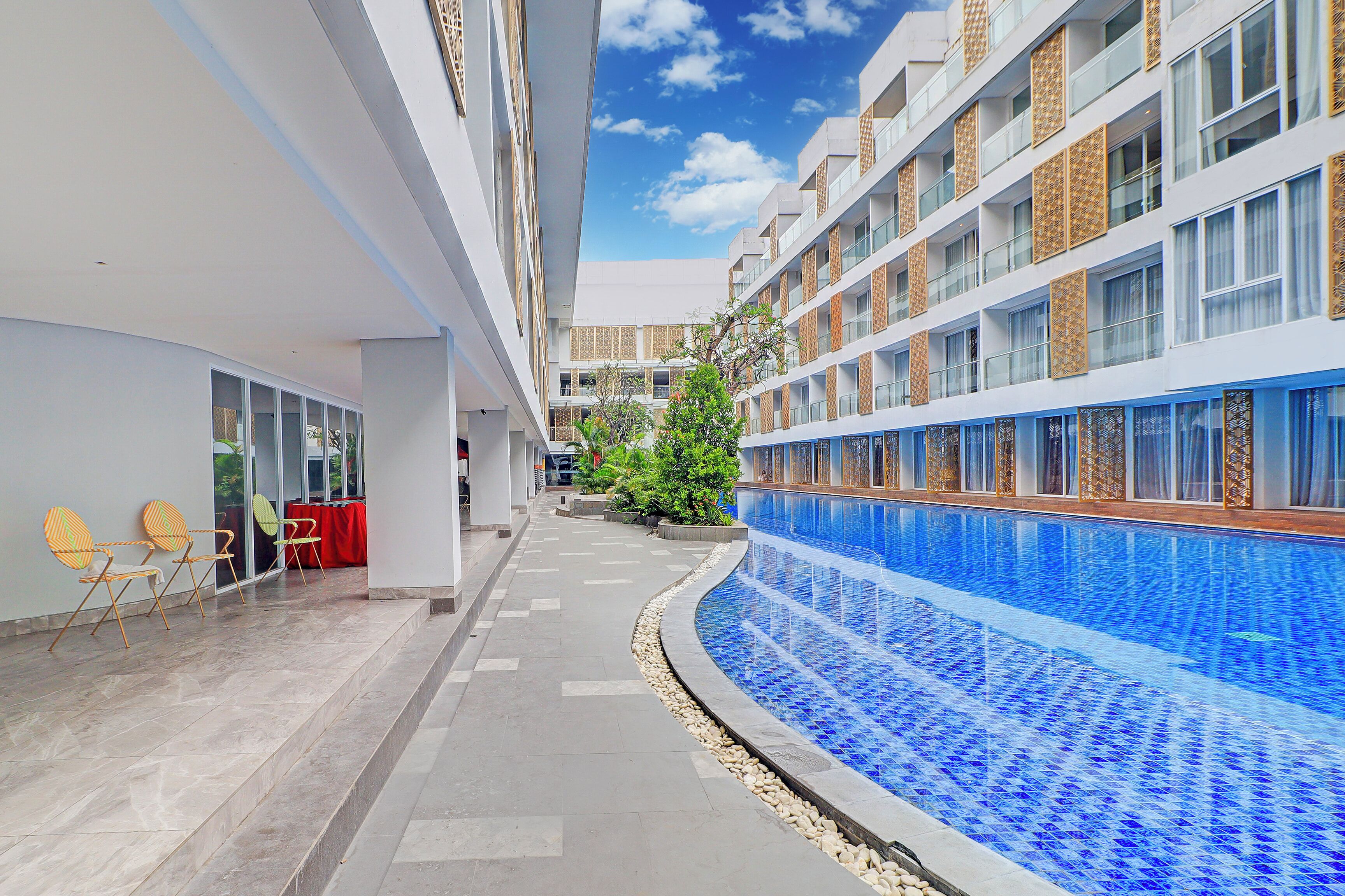 Hotelgang med swimmingpool, udendørs siddepladser og udsigt til himlen.