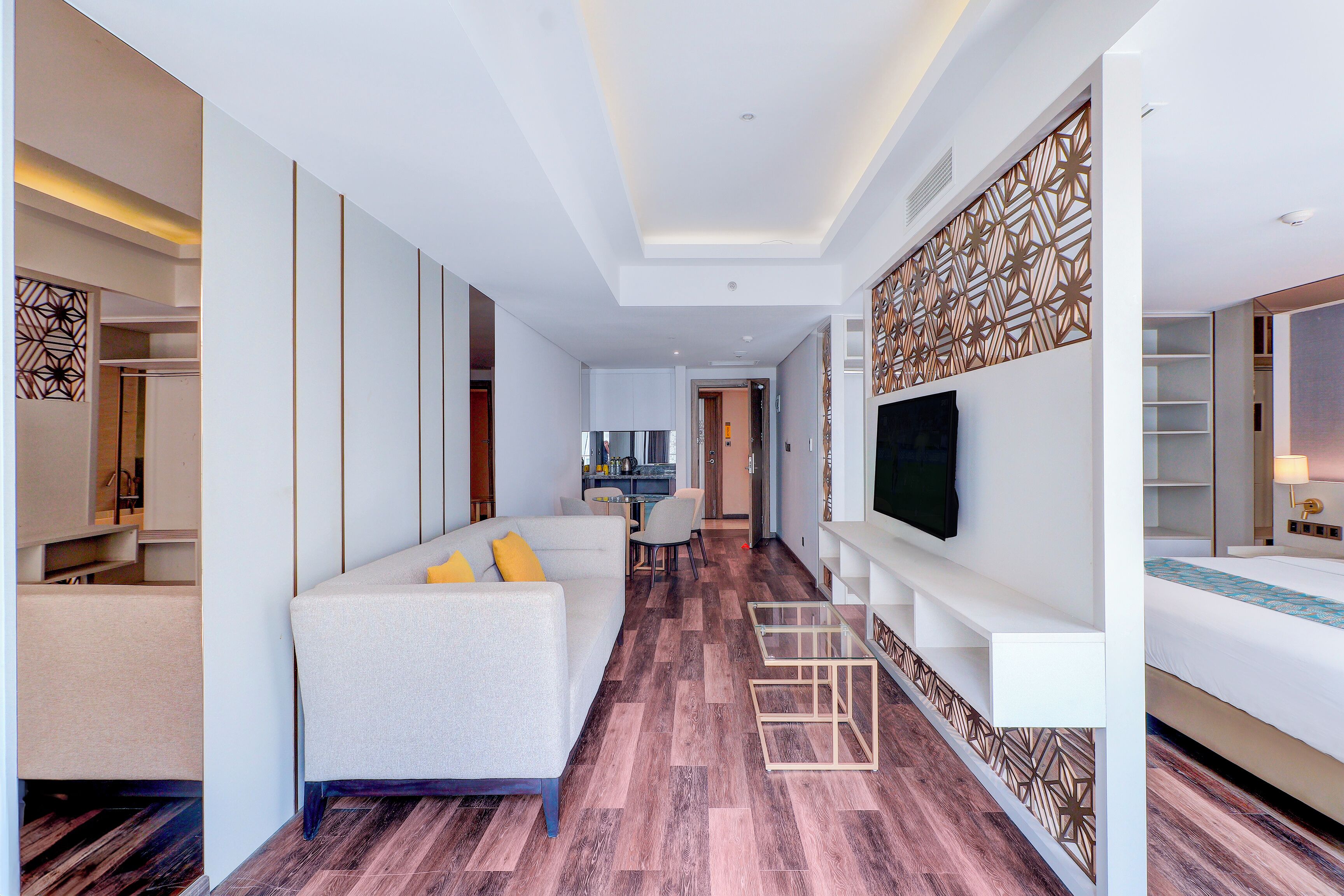A modern hotel room with a sofa, TV, and a dining area.
