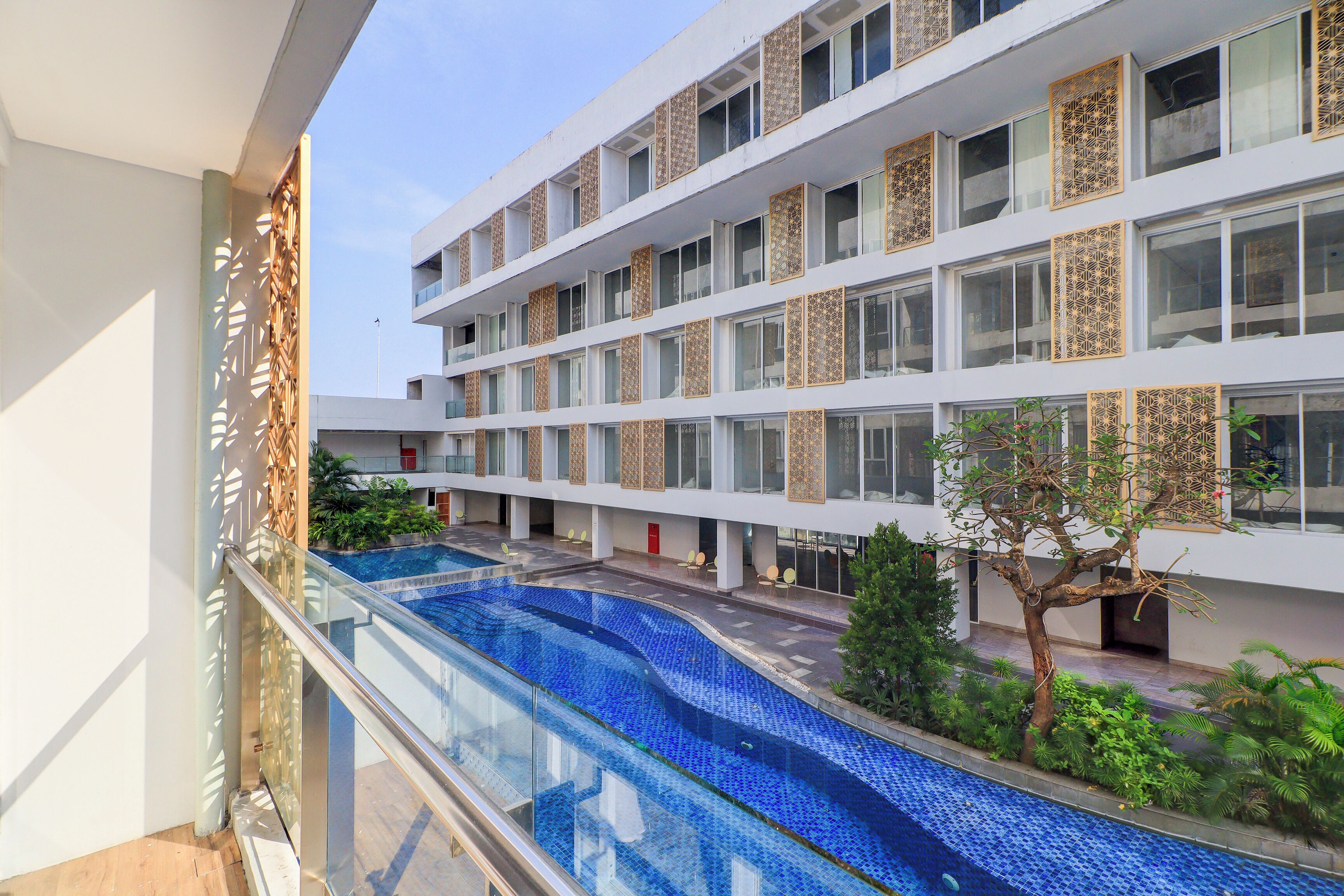 A modern hotel with a large outdoor swimming pool, multiple balconies, and a well-maintained garden area.