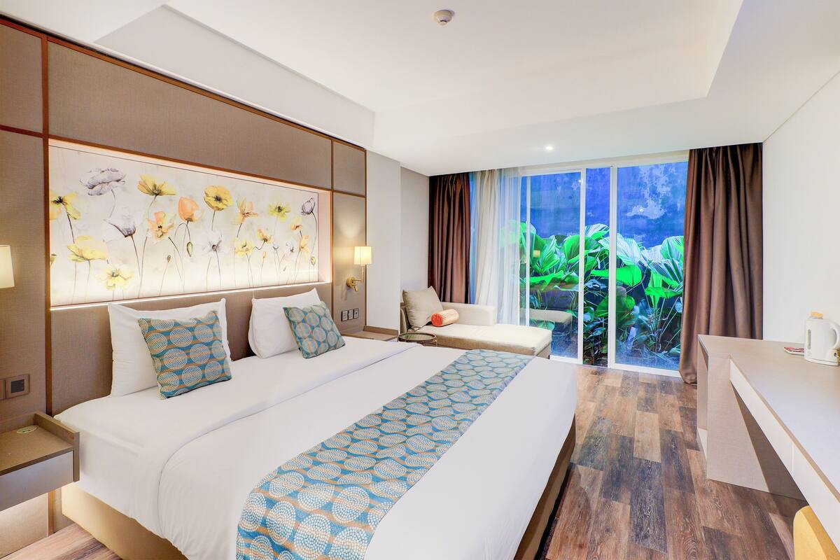 Une chambre d’hôtel avec un grand lit, un bureau et une vue sur la verdure par la fenêtre.