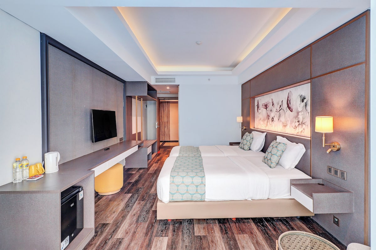 Une chambre d’hôtel moderne dotée d’un grand lit, d’un téléviseur à écran plat, d’un bureau avec un ordinateur et d’une lampe fixée au mur.
