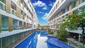 Een modern hotel met een centraal gelegen zwembad, meerdere balkons en weelderige begroeiing.