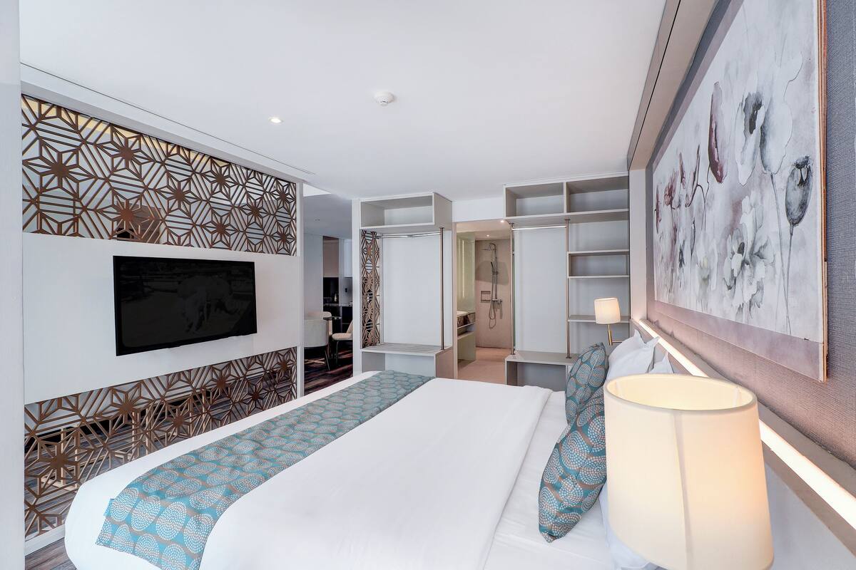 Une chambre d’hôtel moderne avec un grand lit, un téléviseur fixé au mur, un panneau décoratif et un tableau.