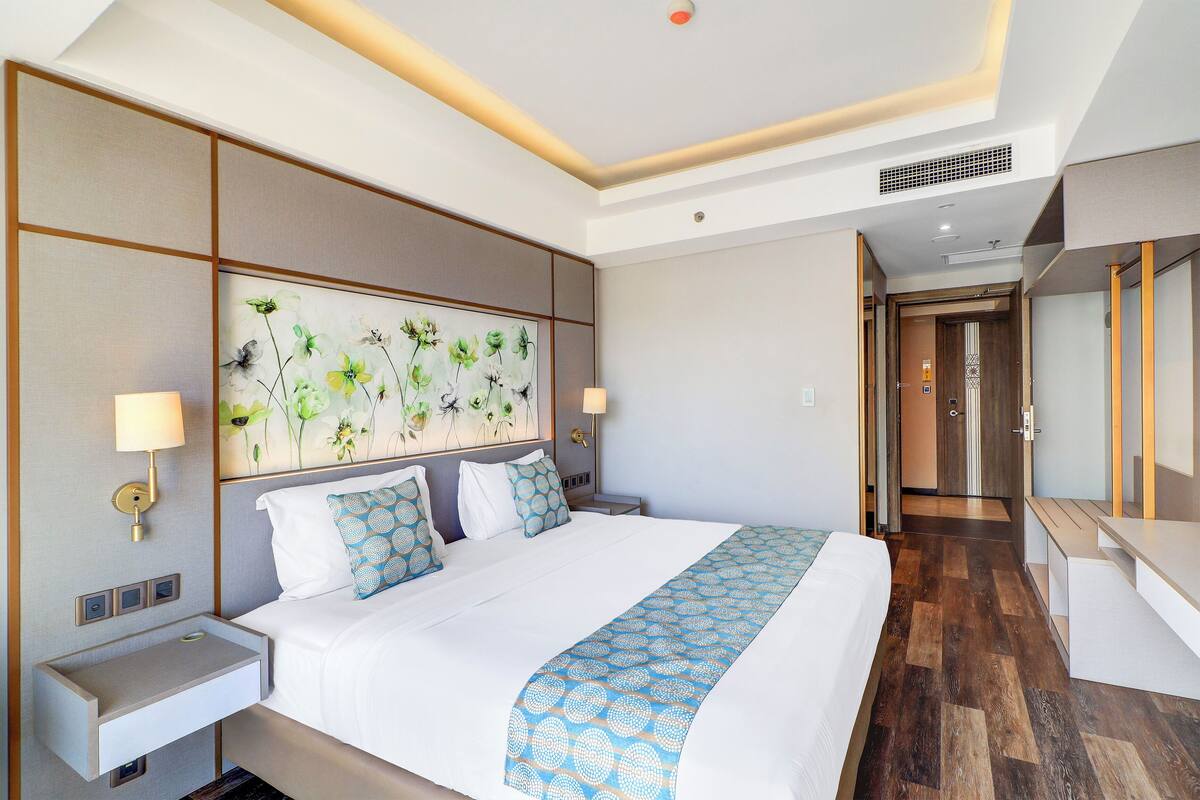 Une chambre d’hôtel avec un grand lit, des tables de chevet, une œuvre d’art accrochée au mur et un plancher en bois.