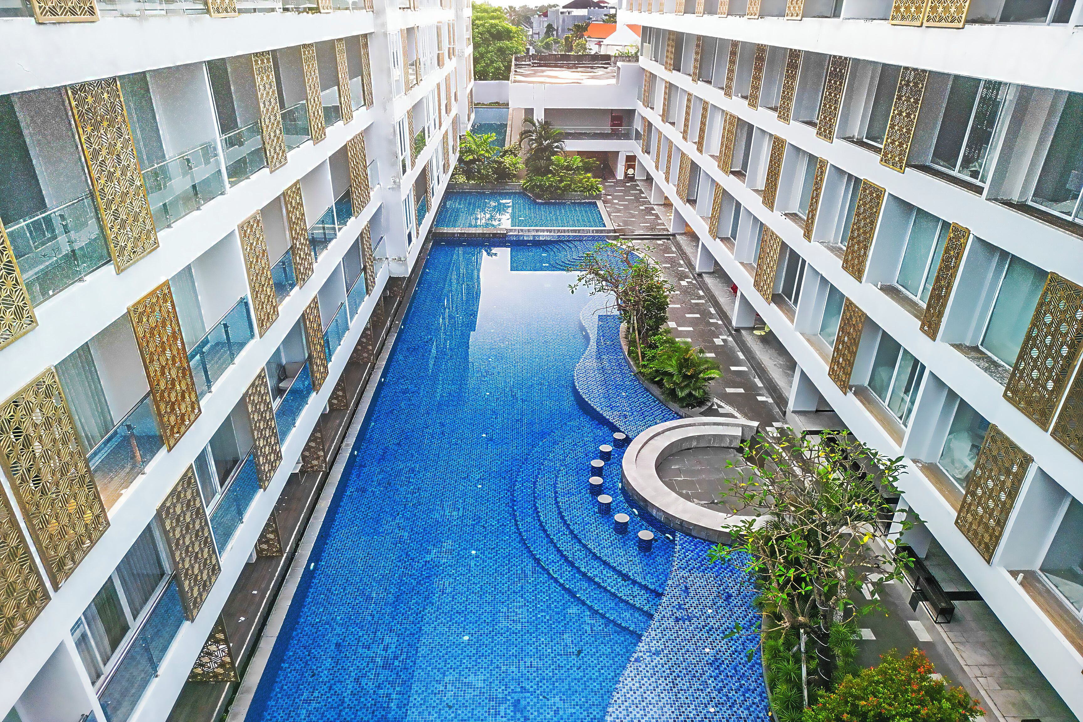 Un hotel de varios niveles con una piscina central, rodeado por balcones con barandillas ornamentadas.