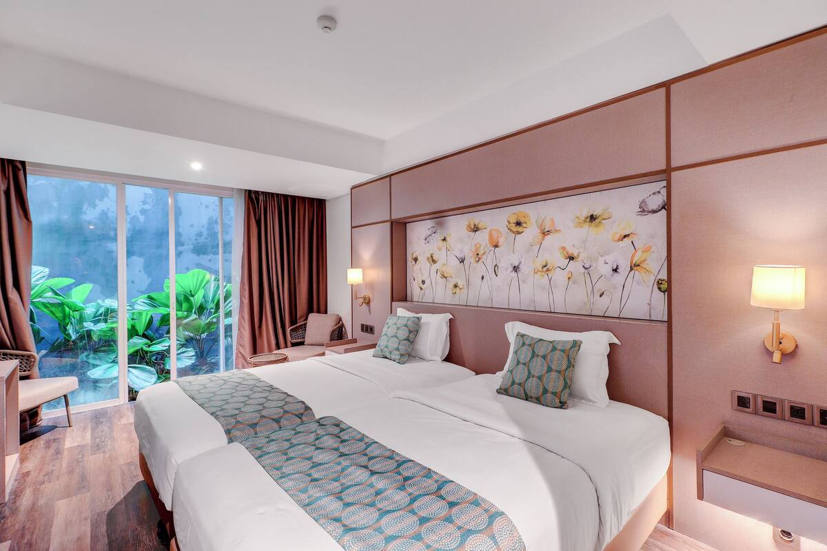 Une chambre d’hôtel avec un grand lit, un bureau et une vue sur la verdure, accessible par une porte-fenêtre coulissante.