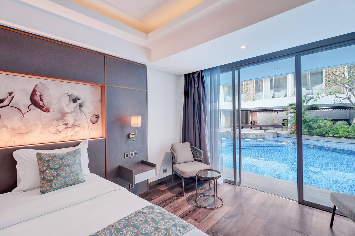 Une chambre d’hôtel avec un grand lit, une chaise, une petite table et une vue sur une piscine.