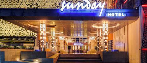 L’extérieur du Sunday Hotel se distingue par sa façade moderne, un grand panneau lumineux et un hall d’entrée bien éclairé.
