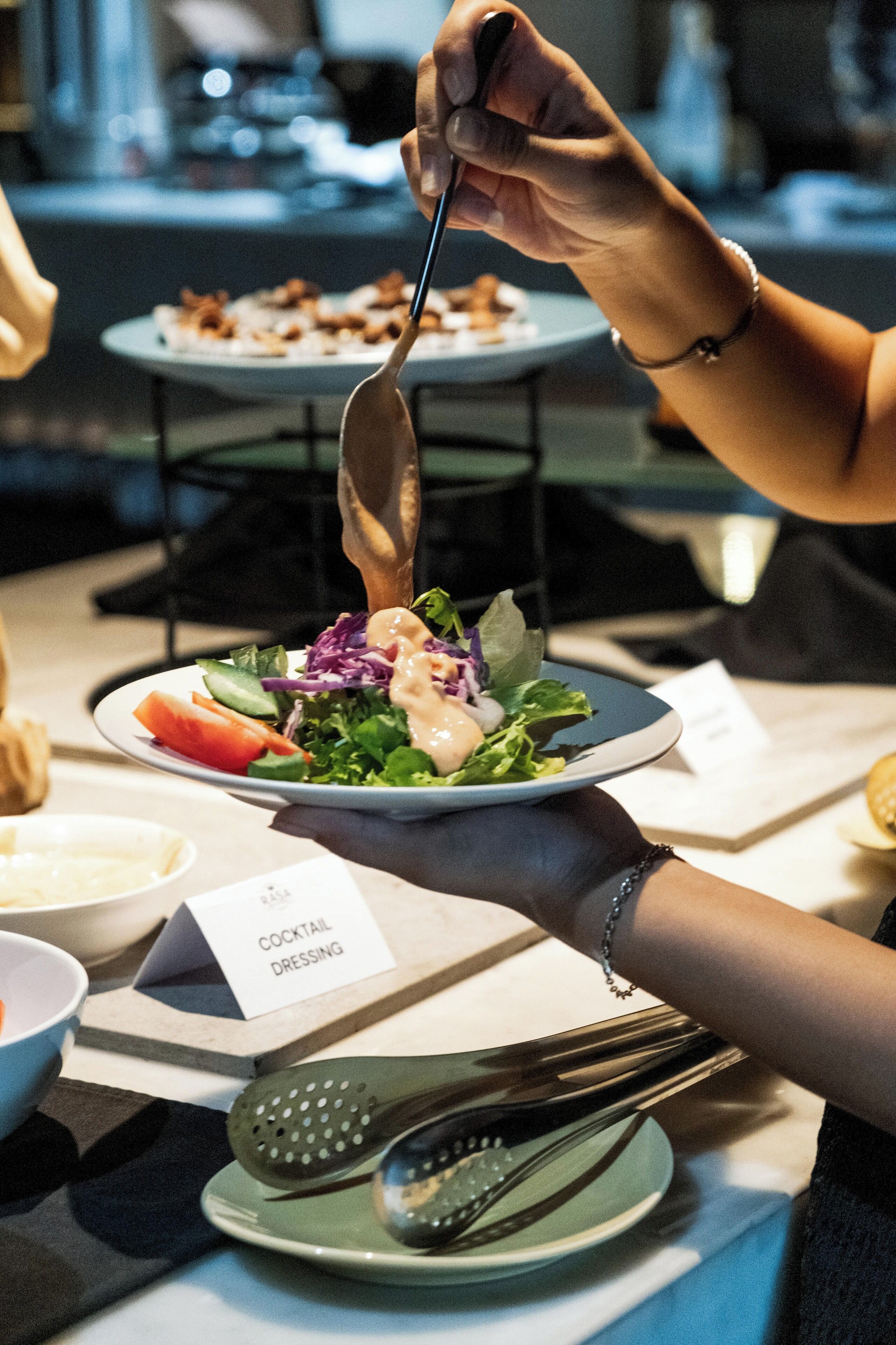A person serving a salad with a cocktail dressing sign on the table.