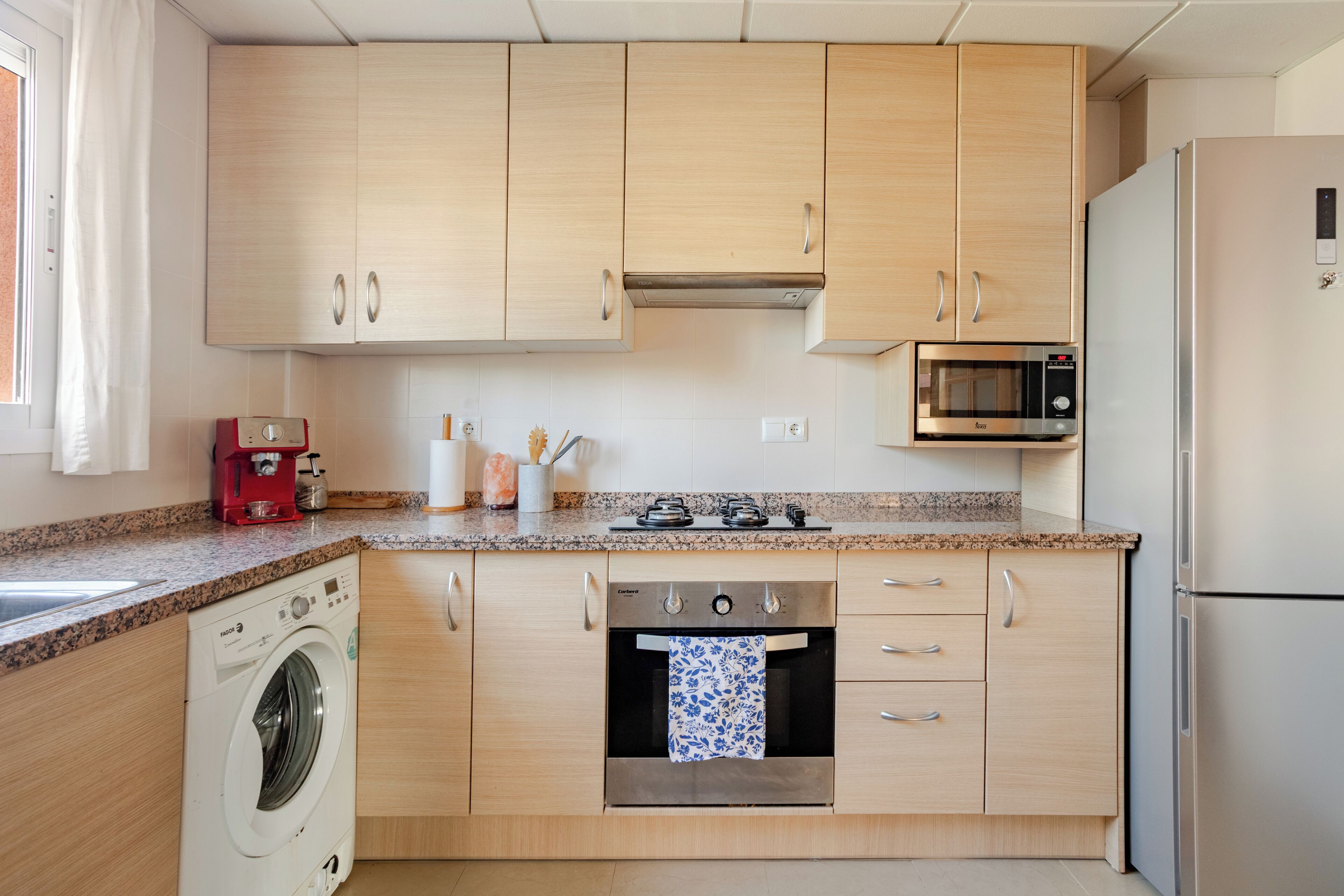 Une cuisine compacte avec des meubles en bois, un lave-linge encastré, un four à micro-ondes et un réfrigérateur.