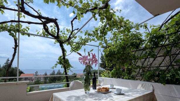 A terrace with a table set for two, a vase with flowers, and a bottle of wine. - Dolac Green Side Apartments (Jelsa)