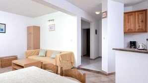 A room with a bed, a sofa, a small table, a kitchen area with a coffee maker, and a cabinet. - Dolac Green Side Apartments (Jelsa)