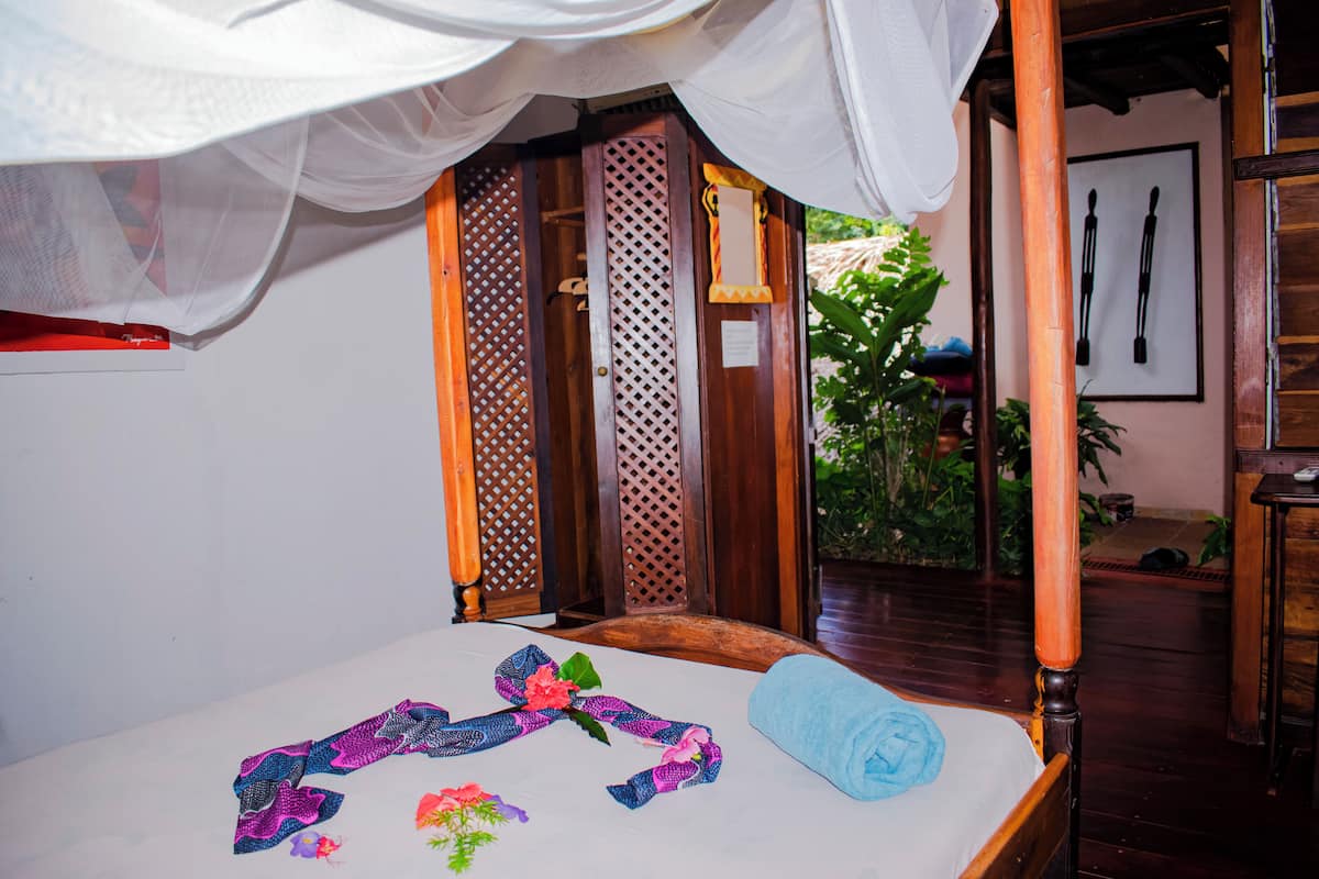 Una habitación con cama, dosel y puerta de madera con diseño de celosía.