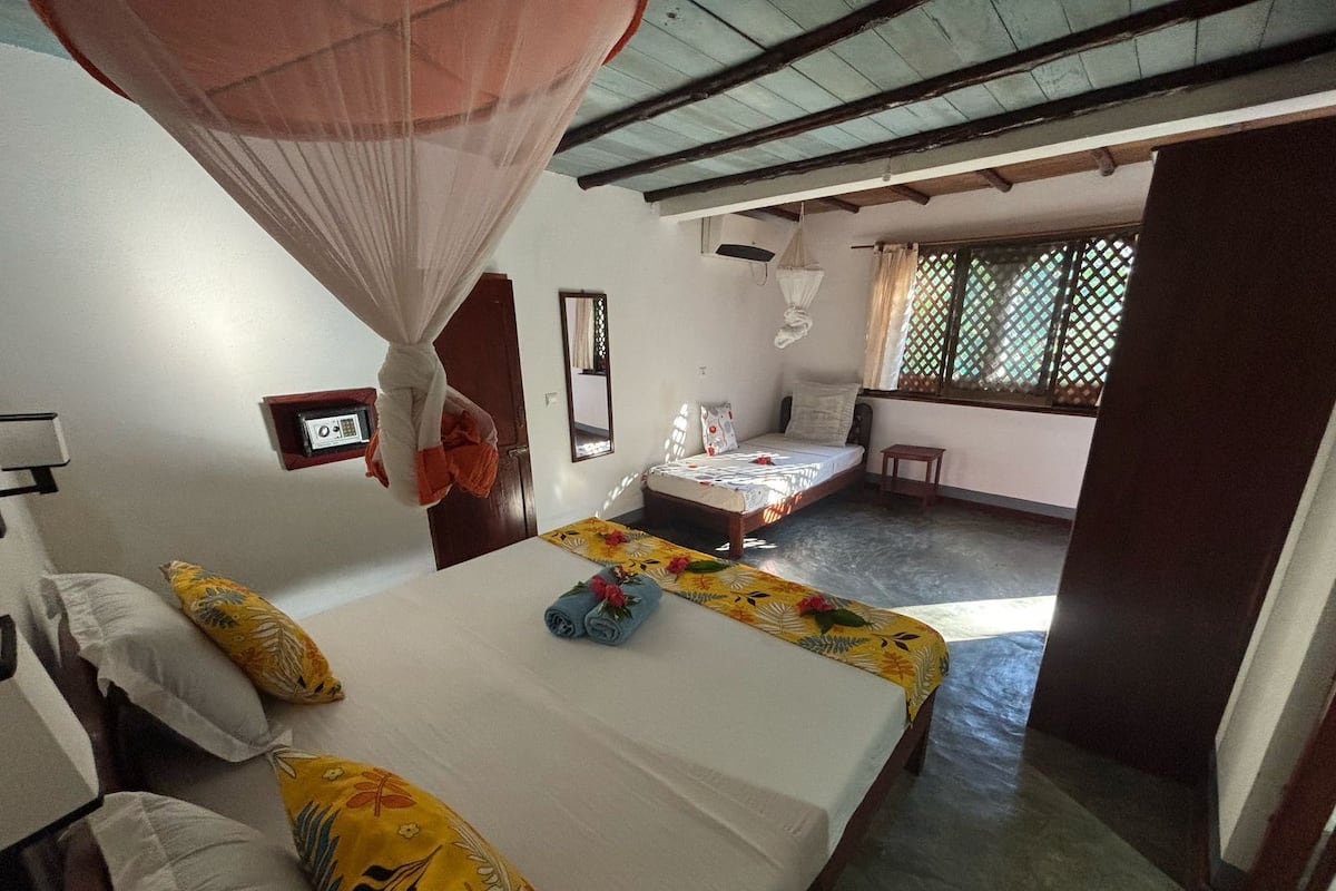 Una habitación con una cama, una mesita de noche, una mosquitera y una ventana con diseño de celosía.