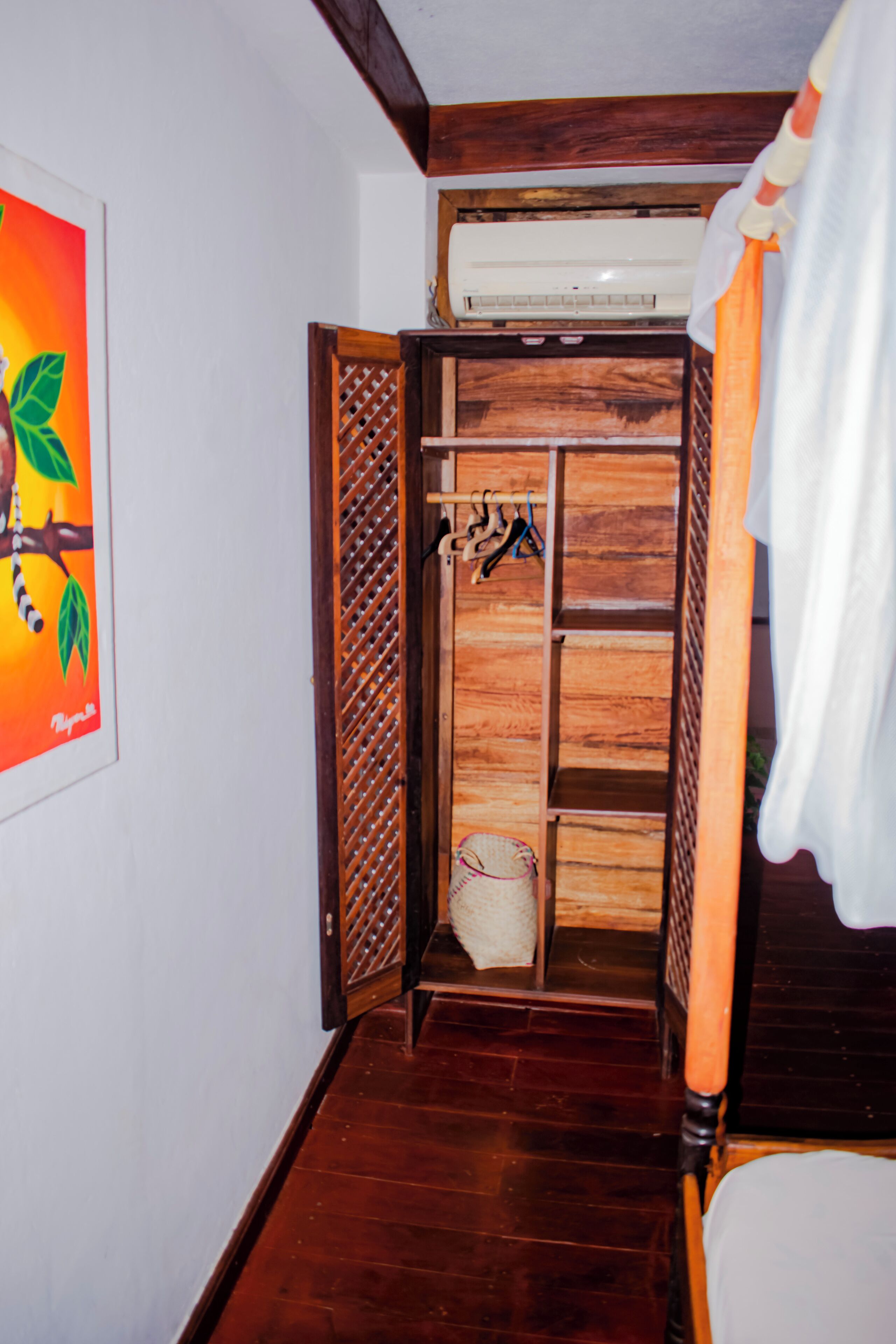 A wooden wardrobe with a hanging rack, a white air conditioning unit above it, and a white curtain to the right.