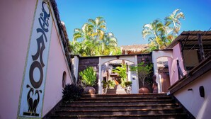 A staircase leading to a building entrance with a thatched roof, surrounded by palm trees and potted plants. - Hotel Restaurant Les Boucaniers (Nosy Be)