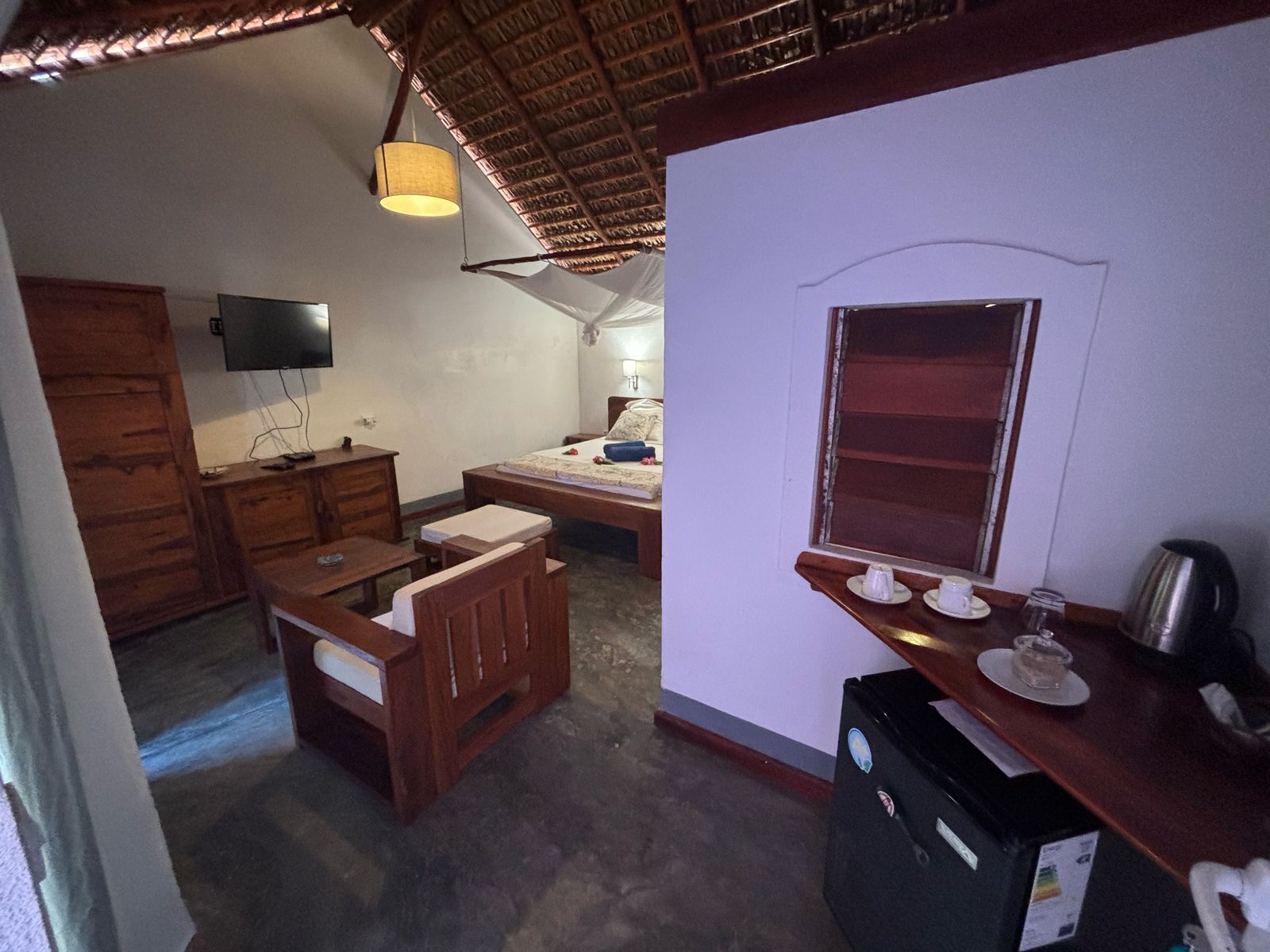 A compact room with a bed, a desk, a chair, a TV, and a kitchenette area.