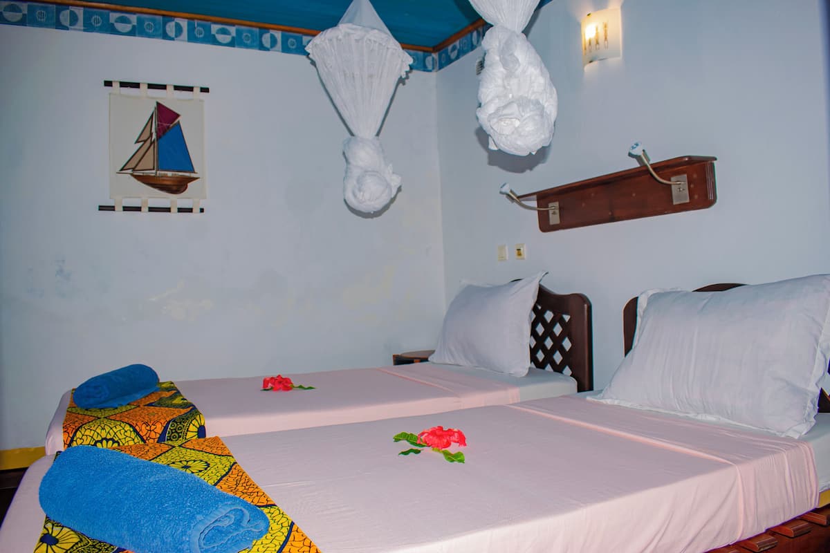 Habitación de hotel con dos camas, cada una con cubrecama y almohadas blancas, cabeceros de madera y estante adosado a la pared.