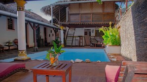 A pool area with a wooden table and lounge chairs, a staircase leading to an upper level, and a stone wall. - Hotel Restaurant Les Boucaniers (Nosy Be)