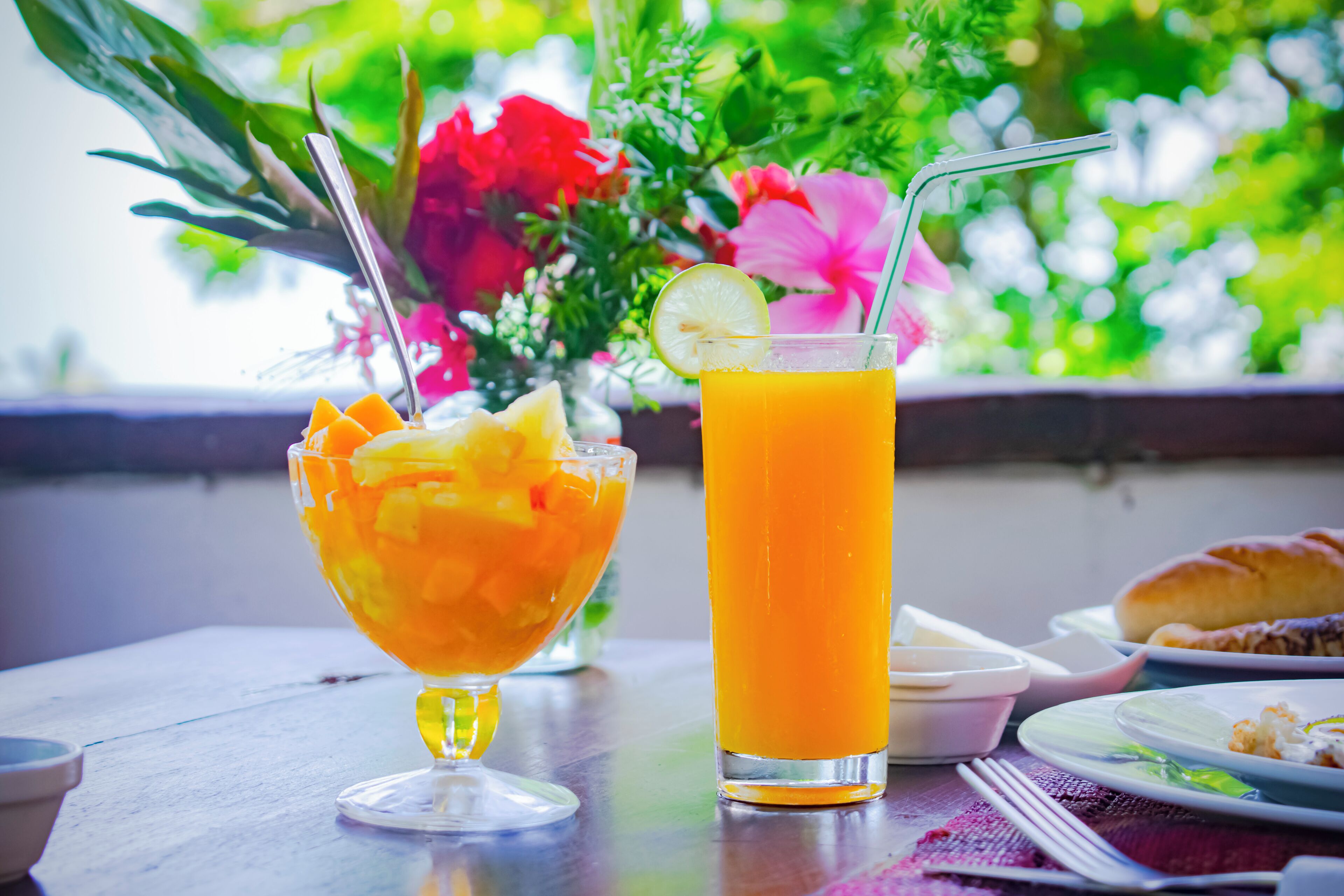 A table with a glass of orange juice, a bowl of fruit, and a plate with food.