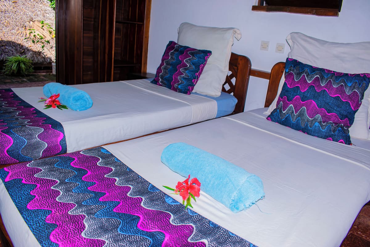 Dos camas individuales con cubrecamas estampados, un cabecero de madera y una ventana pequeña sobre las camas.