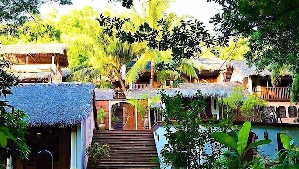 A tropical resort with thatched-roof buildings, a central staircase, and lush greenery. - Hotel Restaurant Les Boucaniers (Nosy Be)