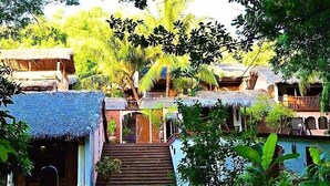 Un resort tropical con edificios de techo de paja, una escalera central y abundante vegetación.