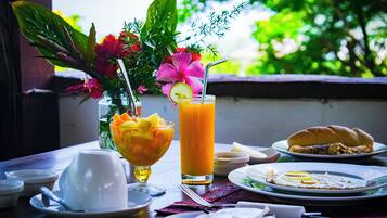 A table set with a glass of orange juice, a bowl of fruit, a plate with food, and a vase with flowers.