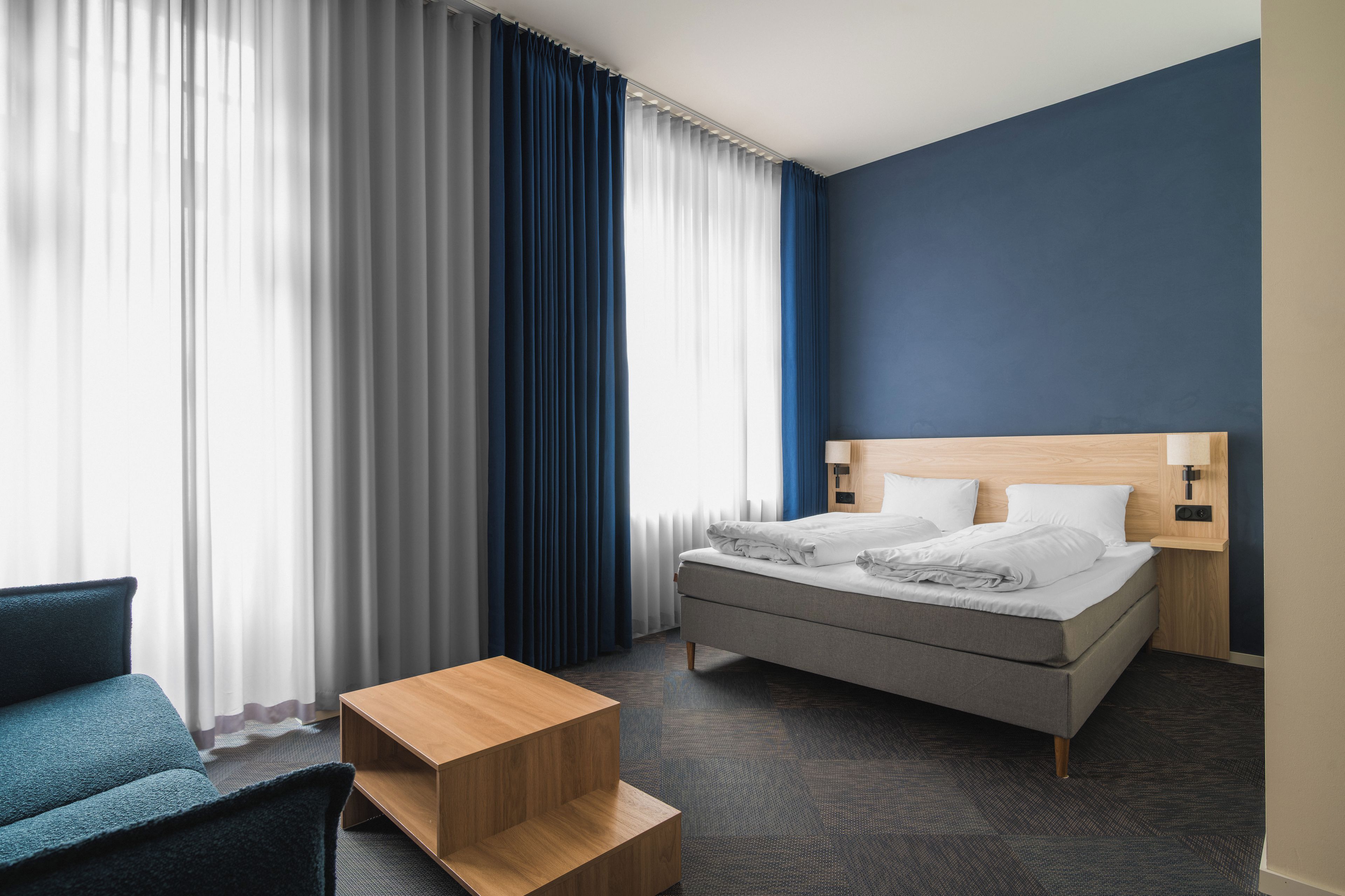 A hotel room with a bed, a desk, a chair, and a window with curtains.