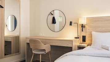 Hotelkamer met een bed, een bureau met stoel, een ronde spiegel en een wandlamp.