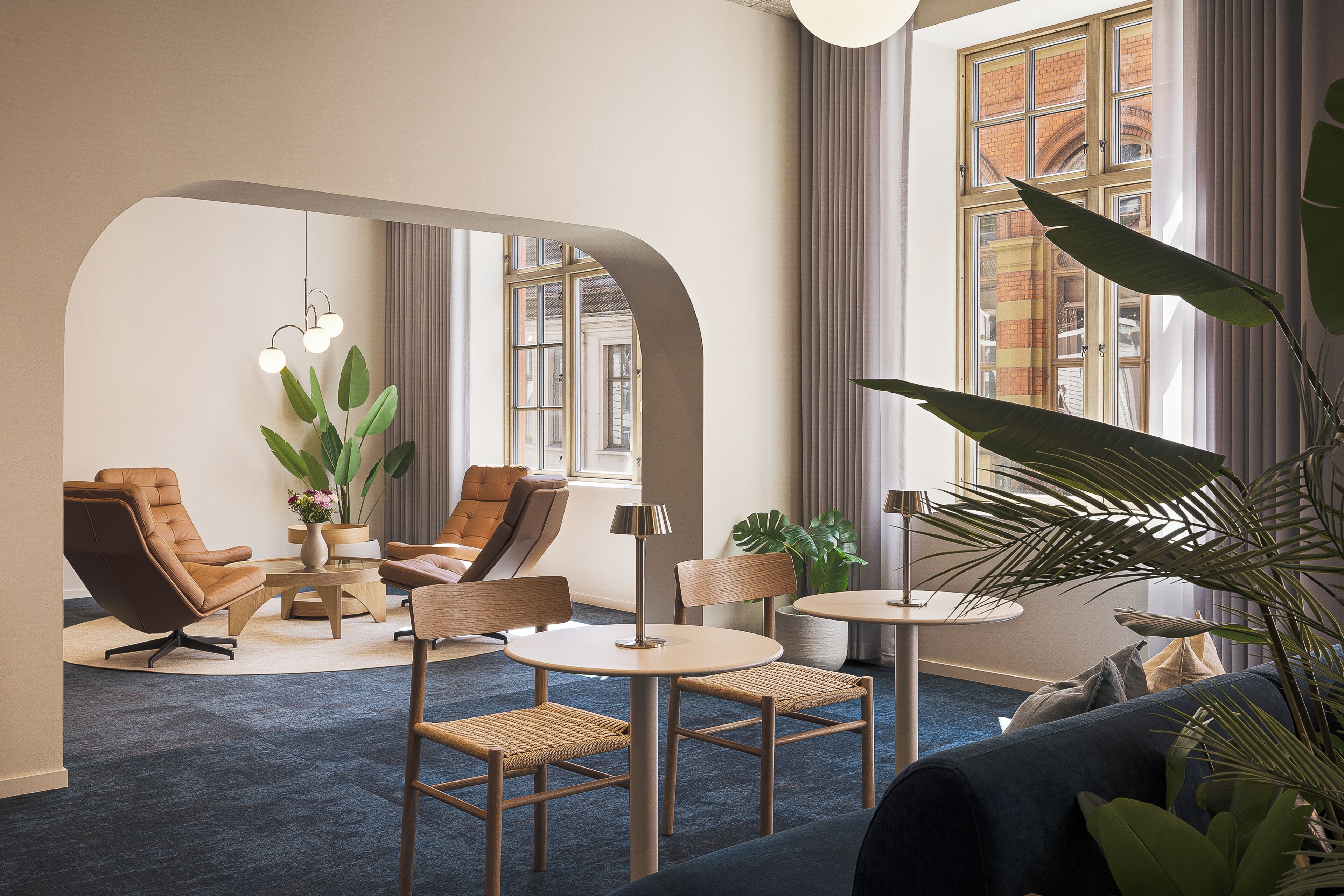 A modern lounge area with leather chairs, a round table, and a large window with curtains.