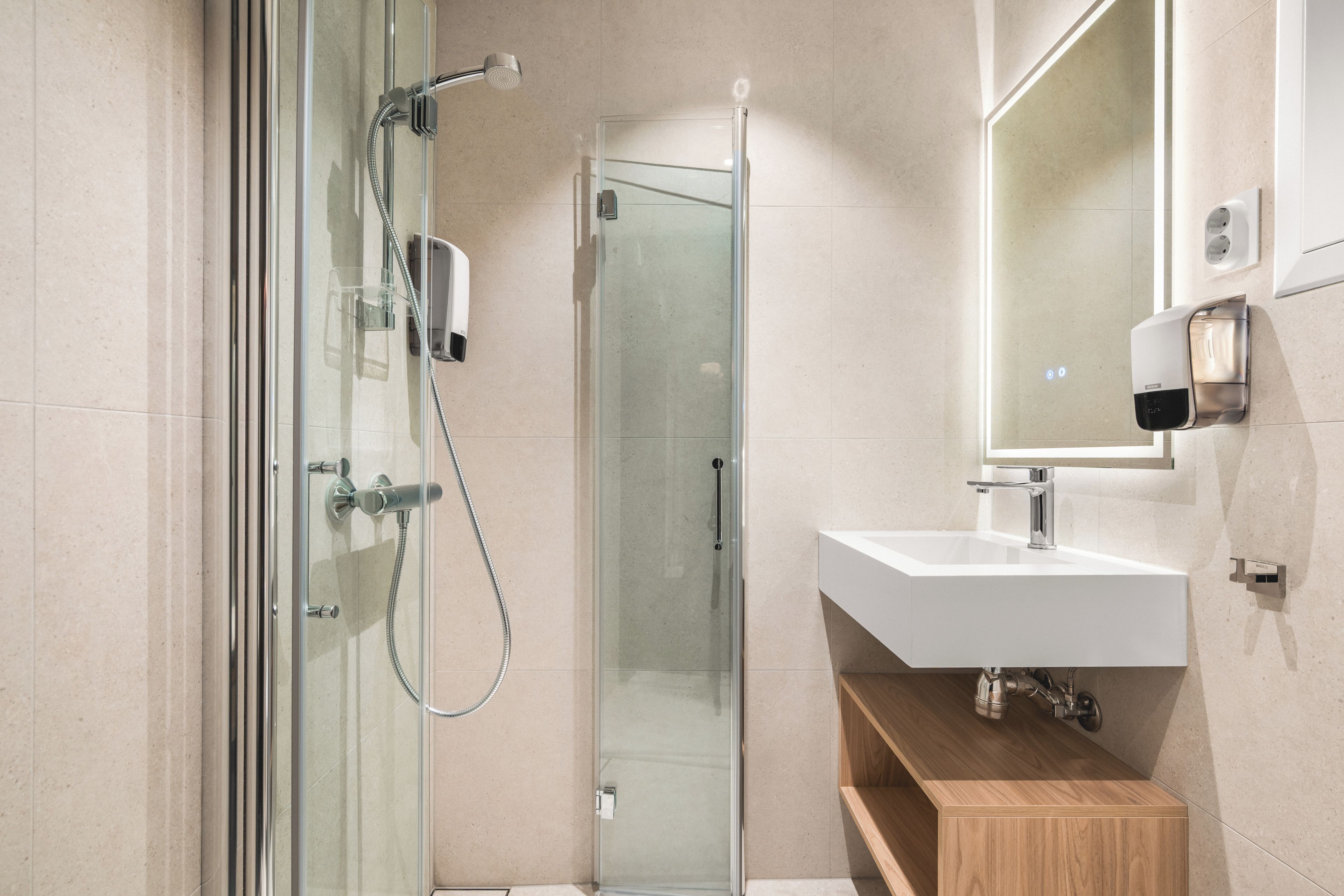 Un baño moderno con ducha envuelta en vidrio, un lavabo blanco y un mueble de tocador de madera.