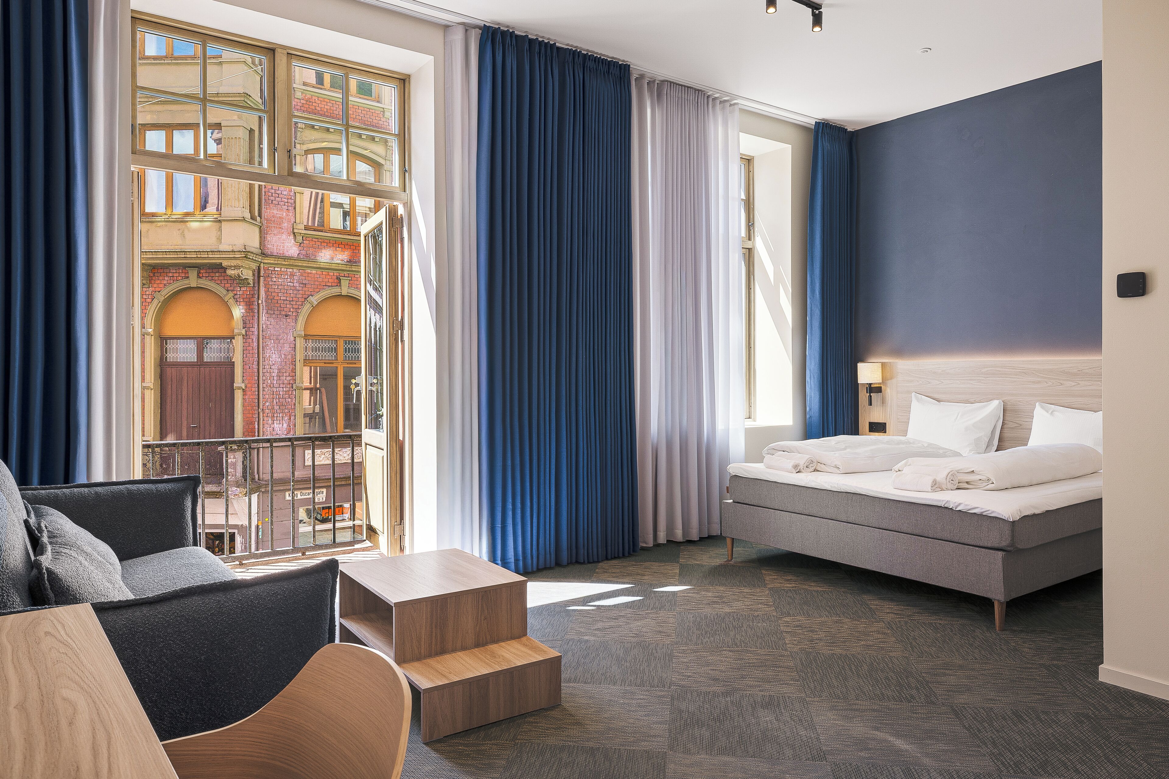 Habitación de hotel con cama, sofá, una mesita y vista a un edificio a través de la ventana.