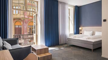 Habitación de hotel con cama, sofá, una mesita y vista a un edificio a través de la ventana.