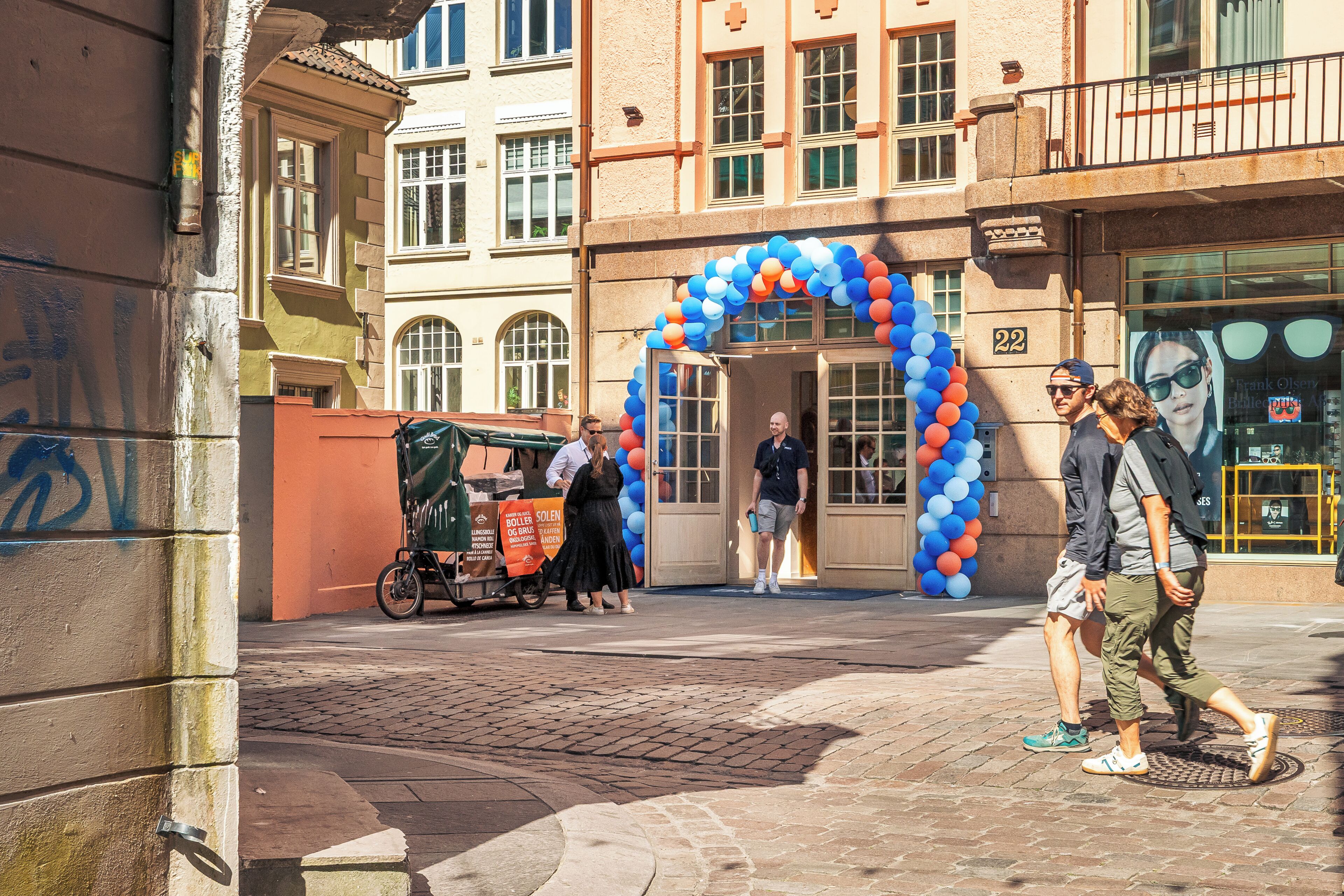 Entrada de um edifício com um arco de balões, uma bicicleta estacionada na frente e uma vitrine com uma grande janela.