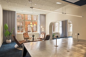 Une salle de conférence moderne, dotée d’une grande table, de fauteuils en cuir et de larges fenêtres avec des rideaux.