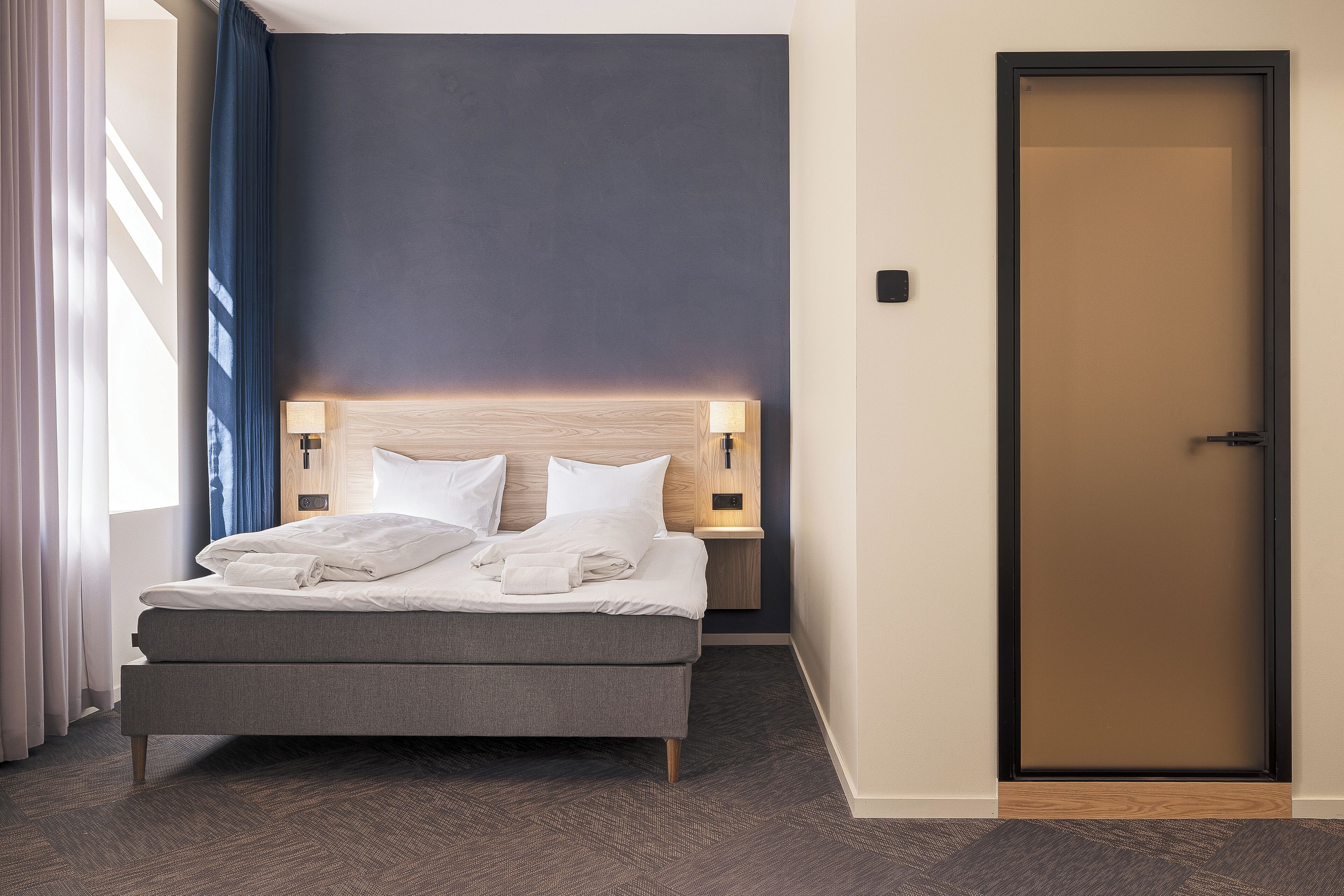 Ein Hotelzimmer mit einem Bett, einem Nachttisch, einer Wandleuchte und einer Tür.