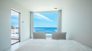 A bedroom with a large window offering a view of the sea and a distant building. - BEACH TERRACE KUSHIMOTO (Kushimoto)