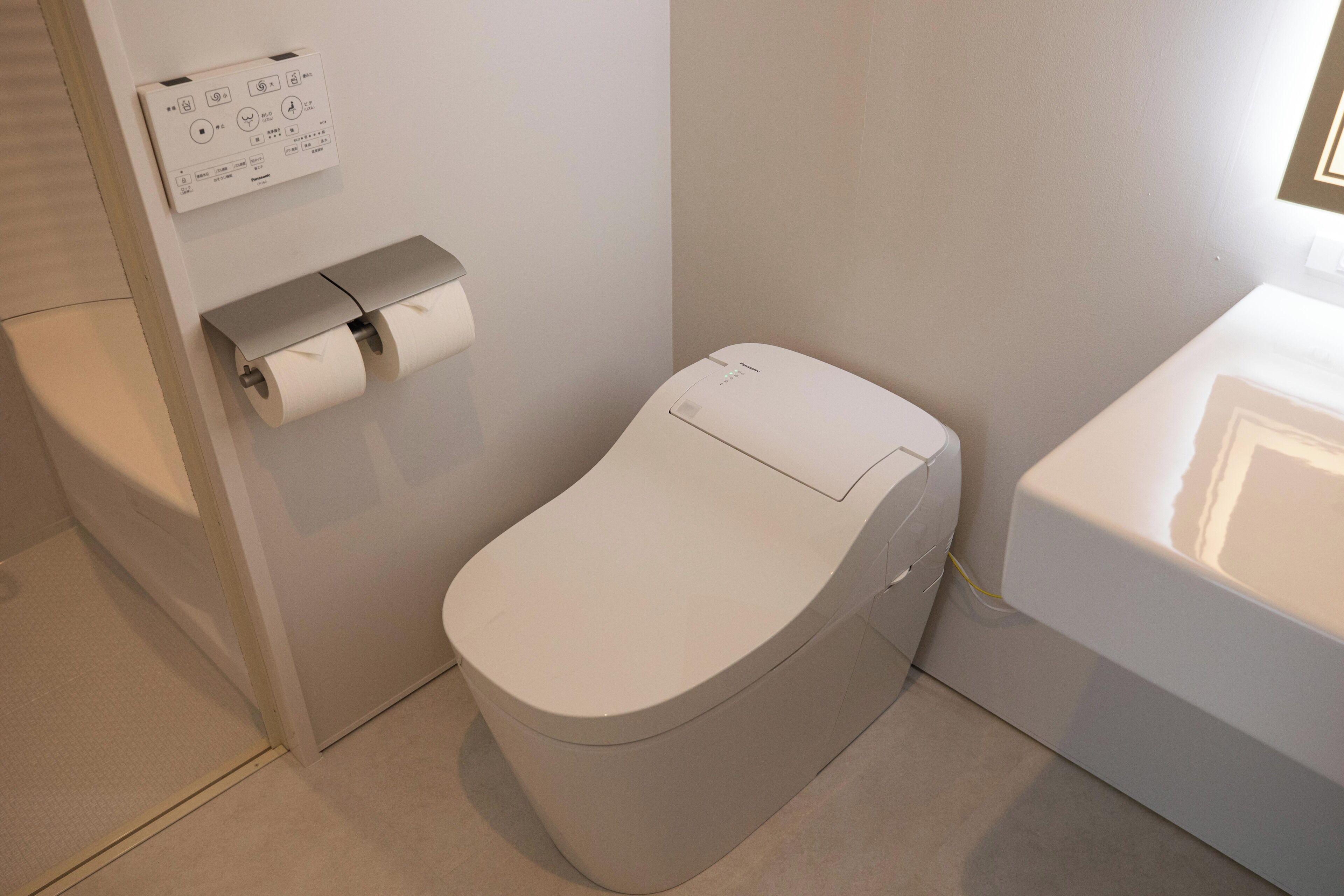 Un baño moderno con inodoro, dispensador de papel higiénico y panel de control en la pared.