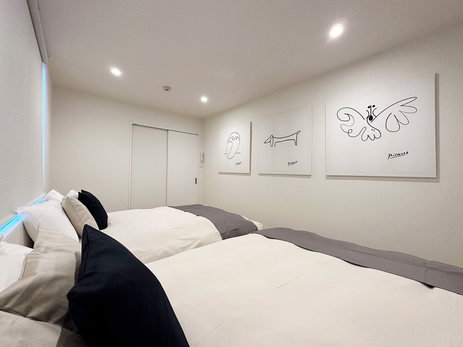 Une chambre d’hôtel moderne avec deux lits, une armoire et trois œuvres d’art encadrées accrochées au mur.