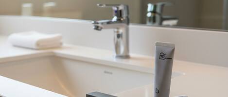 Un baño moderno con un lavabo blanco, un espejo y un portalapices para cepillos de dientes.