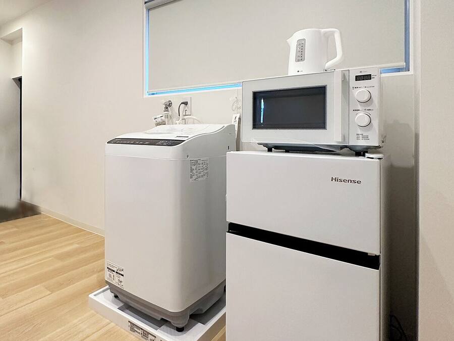 A clean, modern room with a Hisense microwave and refrigerator, wooden flooring, and a plain white wall.