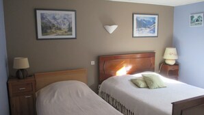A hotel room with two beds, a wooden headboard, a nightstand with a lamp, and two framed pictures on the wall.