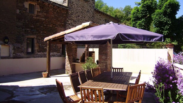 A stone building with a patio table and chairs under a purple umbrella.