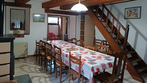 A dining area with a long table, wooden chairs, a staircase, and a ceiling with wooden beams.